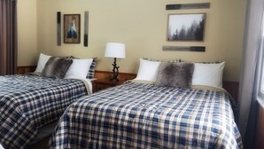 A hotel room with two beds, each with a plaid bedspread, a bedside table with a lamp, and a framed picture on the wall.