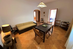 Un espacio habitable compacto con sofá, mesa de comedor, sillas, lámpara y piso de baldosas.