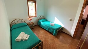 Una habitación pequeña y limpia con dos camas individuales, una mesita de noche, una ventana y una puerta.