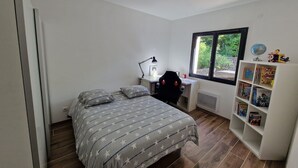 Un dormitorio con una cama, un escritorio, una silla, un radiador, una ventana y una estantería.