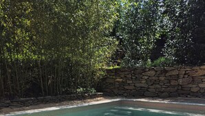 Piscina rectangular con agua cristalina, rodeada de muros de piedra y plantas de bambú.