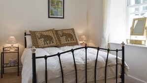 A bedroom with a bed, two bedside lamps, a framed picture on the wall, and a window with a mirror.
