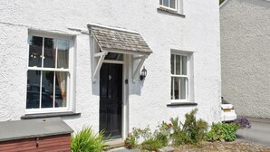 A white two-story house with a black front door, a small porch, and a garden with plants and flowers.