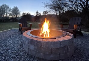 A circular stone fire pit with two Adirondack chairs around it, set on a gravel surface. - Peaceful Retreat w/ Hot Tub, Fire Pit, Mountain Views (Afton)