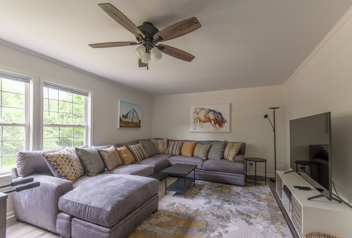 A living room with a sectional sofa, a ceiling fan, a flat-screen TV, and artwork on the walls.