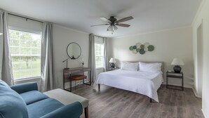 Une chambre à coucher comprenant un lit, un bureau, une chaise, un ventilateur de plafond et une fenêtre avec des rideaux.