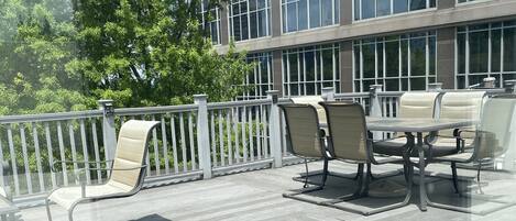 A wooden deck with outdoor seating and a railing, overlooking a modern building with large windows.