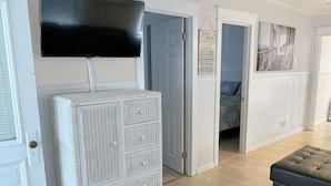 A room with a television mounted on the wall, a white chest of drawers, and a doorway leading to another room. - Cute cottage 300ft to beach, off st parking (Seaside Heights)