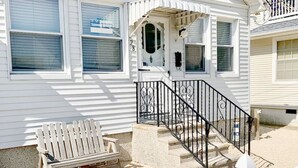 A two-story house with a front porch, a bench, and a staircase with a black railing. - Cute cottage 300ft to beach, off st parking (Seaside Heights)