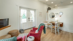 A living room with a TV, a dining area with a table and chairs, and a red chair with a blanket.