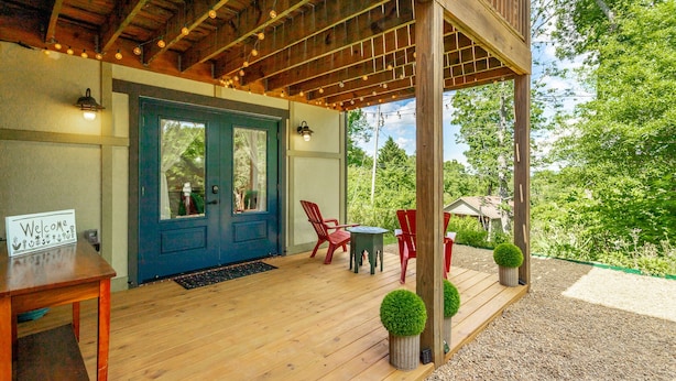 A wooden porch with a blue door, red chairs, and a welcome sign.