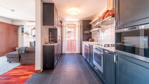 A modern kitchen with dark cabinetry, a built-in oven, and a dining area with a grey sofa.