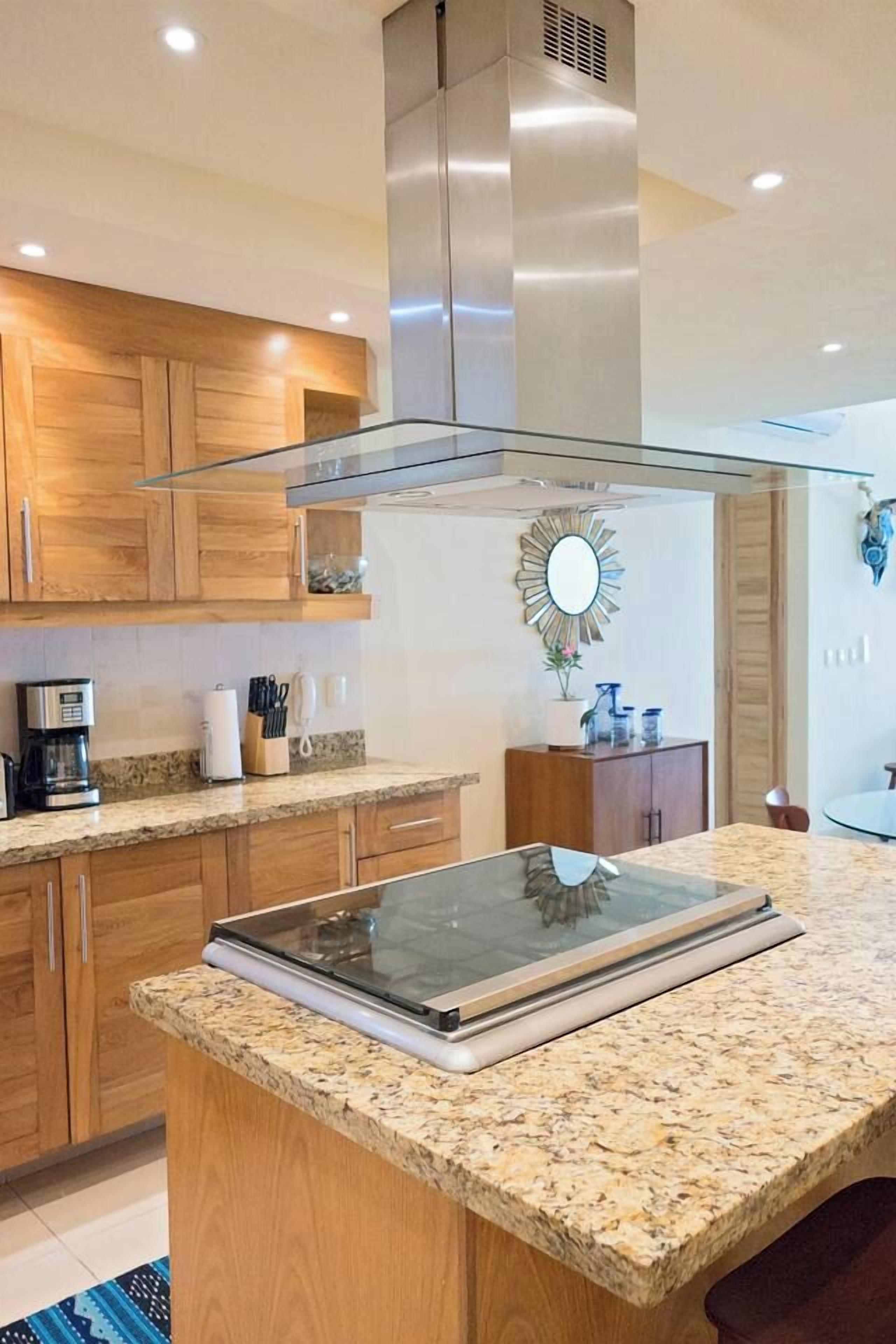 A modern kitchen with wooden cabinets, a granite countertop, and a stainless steel range hood.