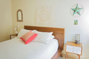 A neatly made bed with white and red pillows, a wooden headboard, a bedside table with a lamp, and a wall with decorative items including a star and a framed picture. - Beautiful, Airy Condo Near Boardwalk**** (Puerto Vallarta)