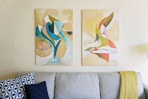 Two abstract paintings on a wall above a grey sofa with patterned cushions.