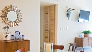 A dining area with a round glass table, wooden chairs, a wooden cabinet, and a decorative mirror on the wall. - Beautiful, Airy Condo Near Boardwalk**** (Puerto Vallarta)