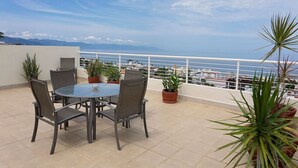 A terrace with a round table and chairs, potted plants, and a view of the sea and buildings. - Beautiful, Airy Condo Near Boardwalk**** (Puerto Vallarta)