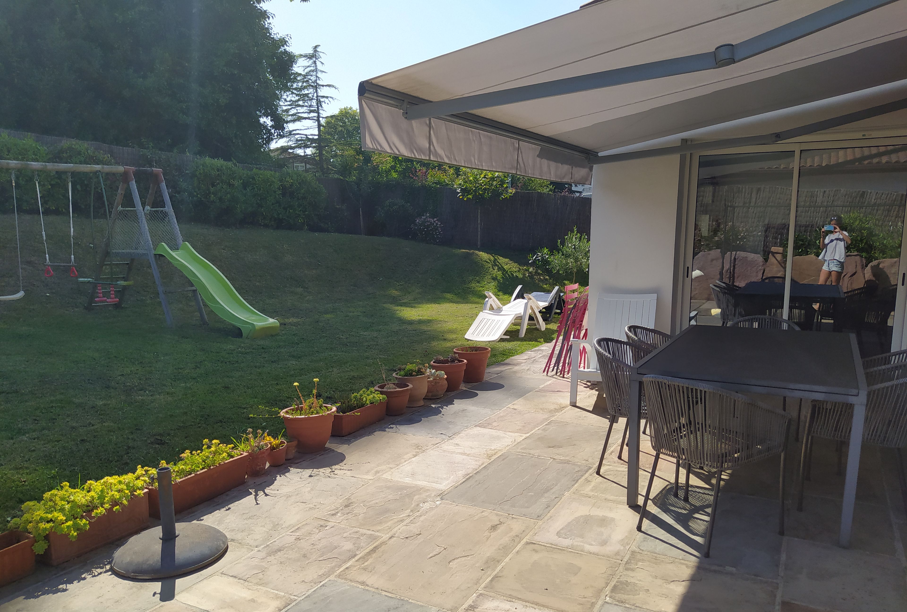 Eine Terrasse mit Tisch und Stühlen, ein überdachter Bereich und ein Spielplatz mit Rutsche.