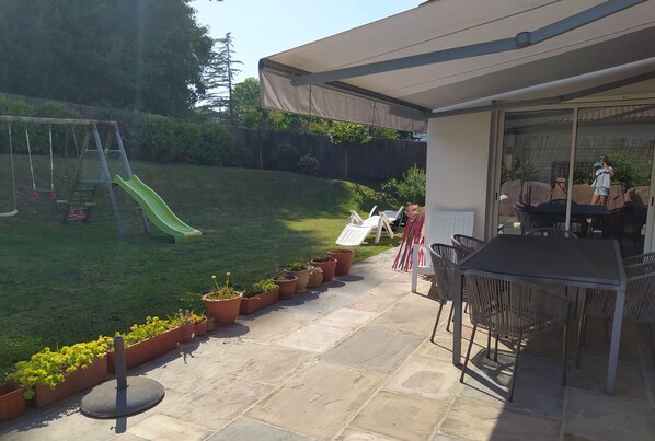 Un patio con una mesa y sillas, un área techada y un parque infantil con tobogán.