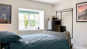 Un dormitorio con cama, ventana, radiador, televisión y perchero.