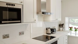 Una cocina moderna con armarios blancos, horno integrado, microondas y cafetera.