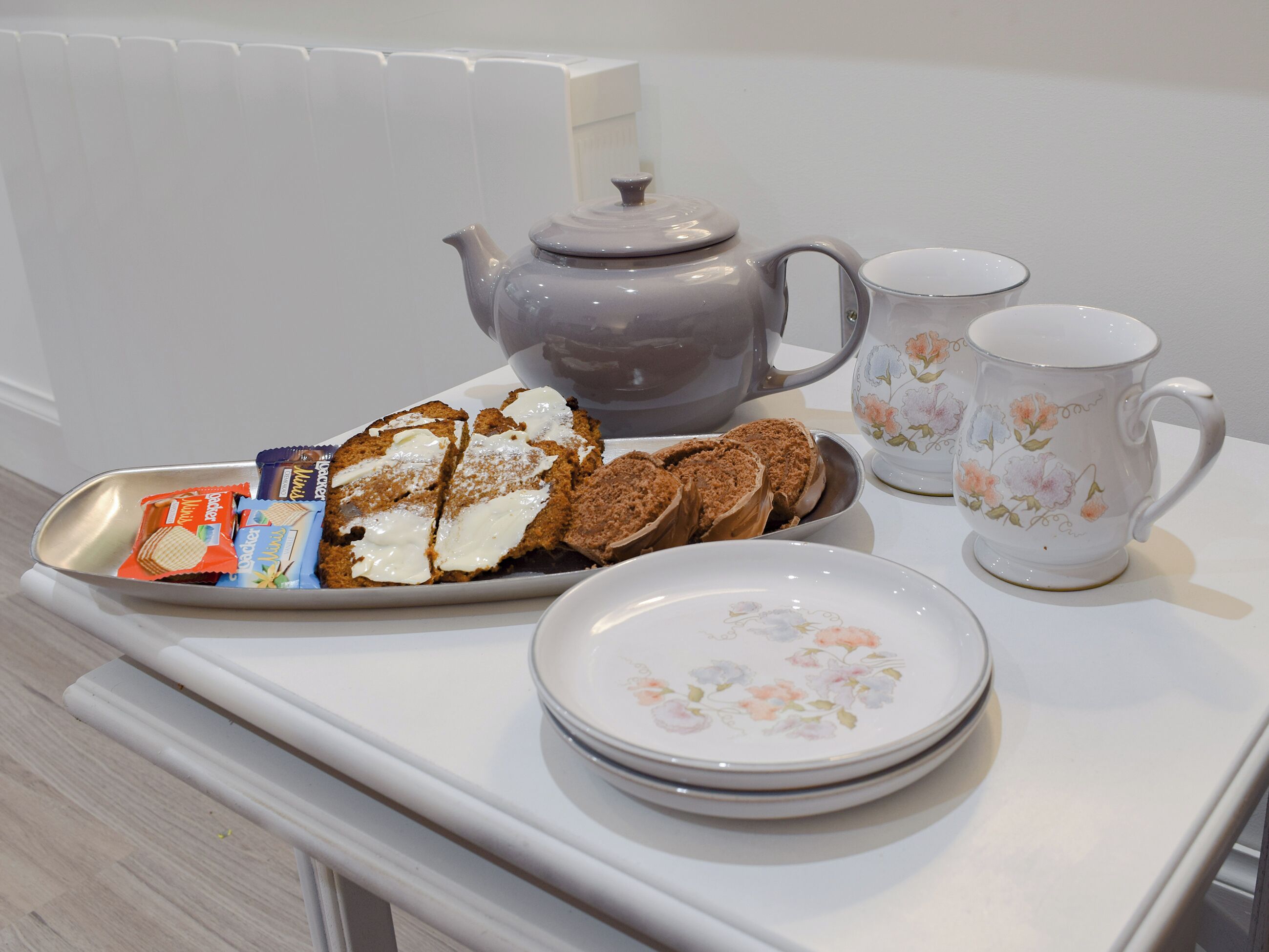 Un esmorzar acompanyat d'una teiera, dues tasses, un plat amb galetes i una safata amb barres de xocolata.