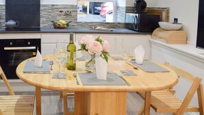 A round wooden dining table set with white napkins, silverware, and wine glasses, surrounded by wooden chairs. - 2 bedroom accommodation in Newburgh, near Cupar (Newburgh, near Cupar)