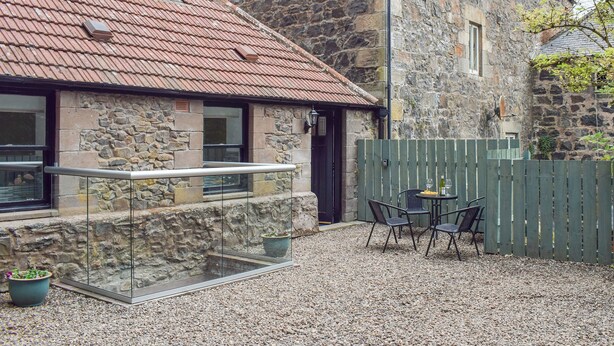 A stone building with a red-tiled roof, a glass balcony, and a gravel patio with outdoor seating. - 2 bedroom accommodation in Newburgh, near Cupar (Newburgh, near Cupar)