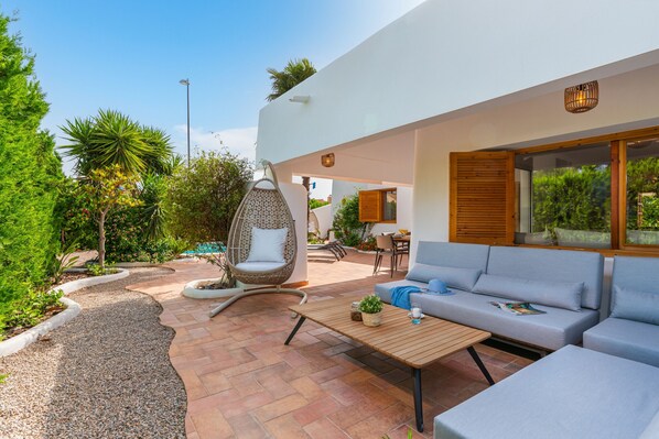 Un'area living esterna moderna con un divano, una poltrona sospesa e un tavolo.