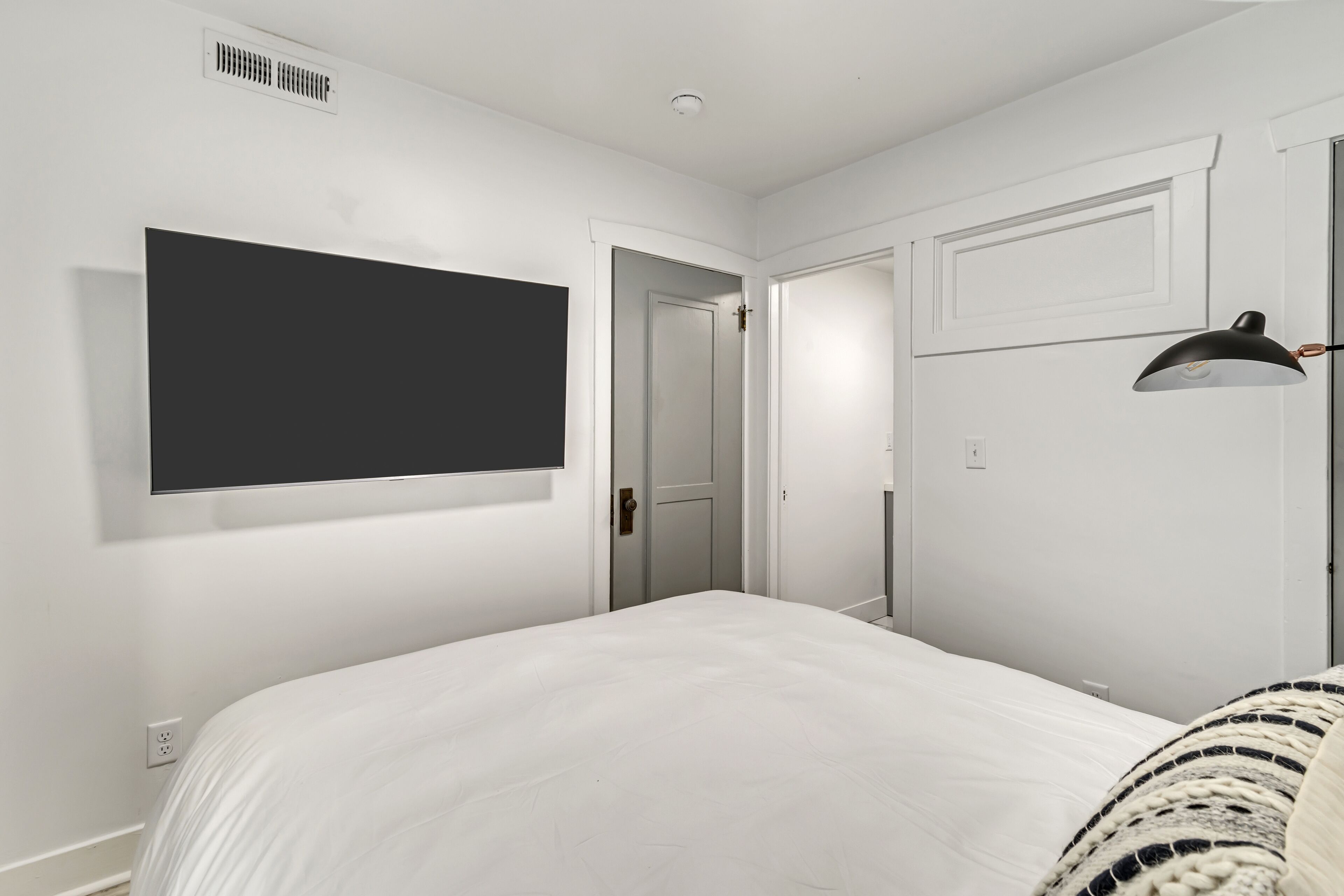 Une chambre à coucher avec un grand lit, un téléviseur fixé au mur, une porte et une lampe.