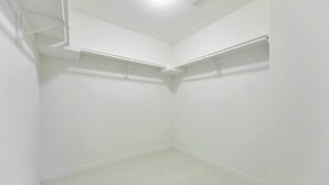 Une pièce blanche et vide, avec un plafond en pente, une étagère d’angle et une prise électrique visible.