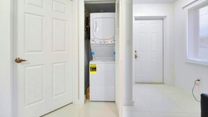 Une buanderie équipée d’un lave-linge et d’un sèche-linge, une porte avec une poignée et une fenêtre sur le côté droit.