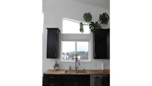 A modern kitchen with black cabinets, a wooden countertop, a sink, and a window with a view of buildings. - Peaceful Homer Getaway (Homer)