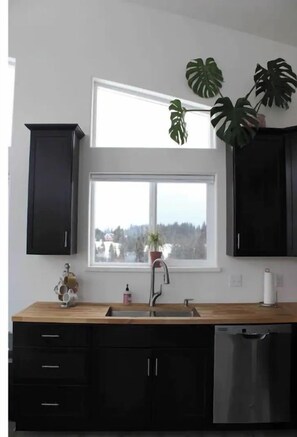 Una cocina moderna con armarios negros, encimera de madera, un lavabo y una ventana con vistas a edificios.
