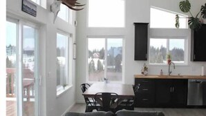A modern kitchen with black cabinets, a dining area with a table and chairs, and a large window offering a view of the outdoors. - Peaceful Homer Getaway (Homer)