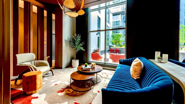 Un salon moderne avec un canapé bleu, un fauteuil blanc et une table basse ronde. Une grande fenêtre offre une vue sur l’extérieur.