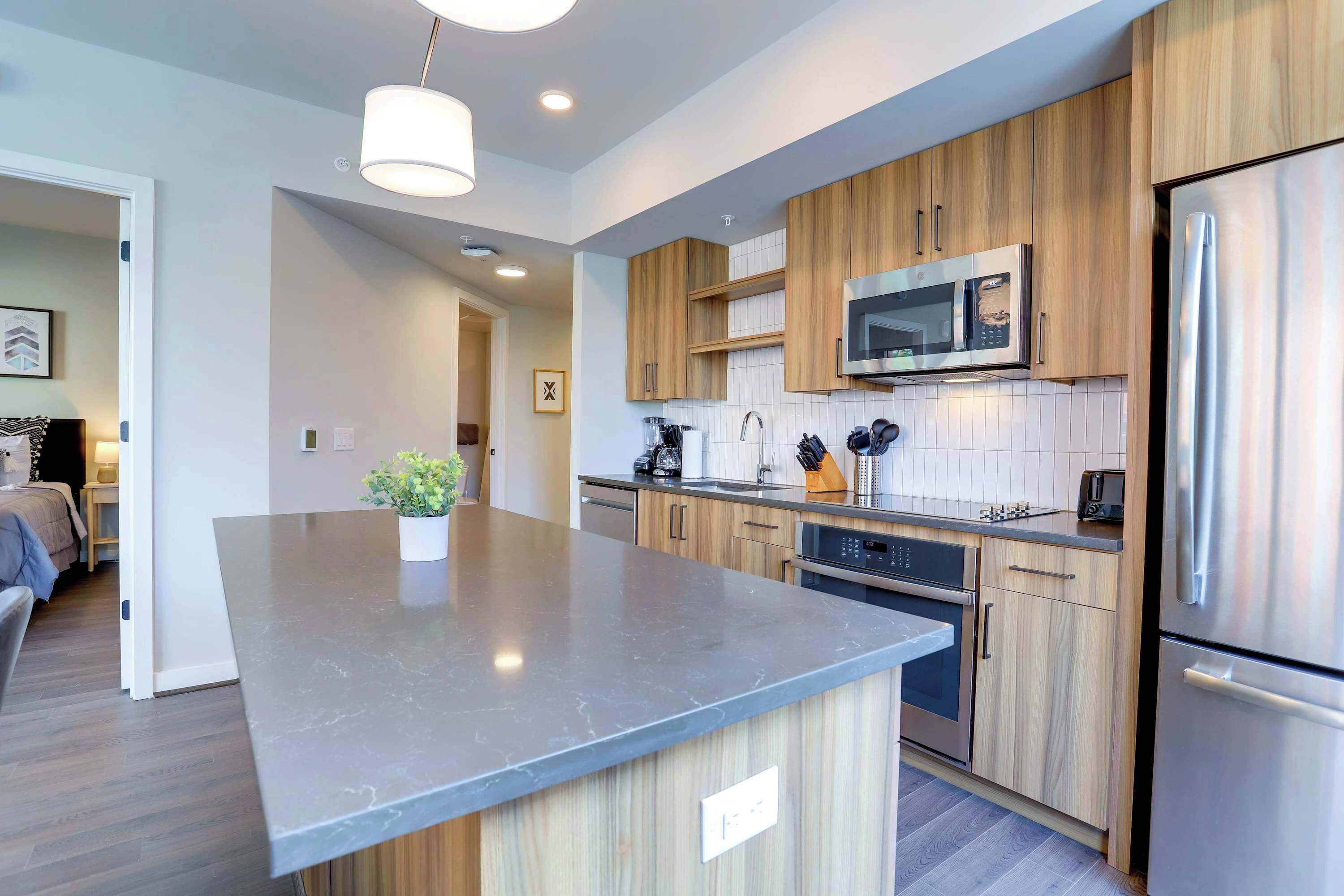 A modern kitchen with wooden cabinets, a large island, stainless steel appliances, and a pendant light.