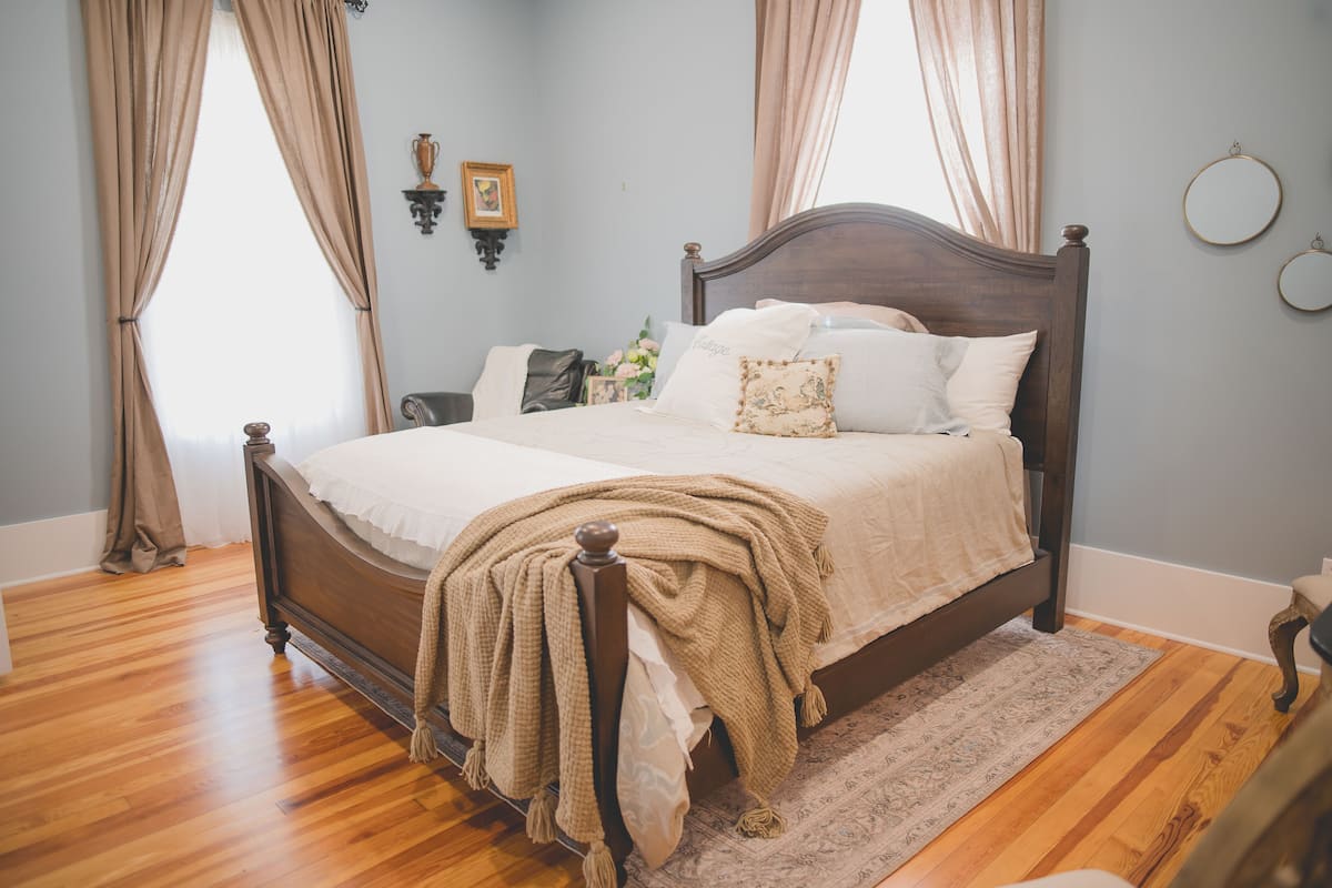 A neatly made bed with a wooden headboard, a beige throw blanket, and a patterned throw.
