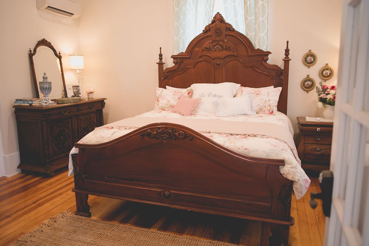 A wooden four-poster bed with floral bedding, a nightstand with a lamp, and a dresser with a mirror.