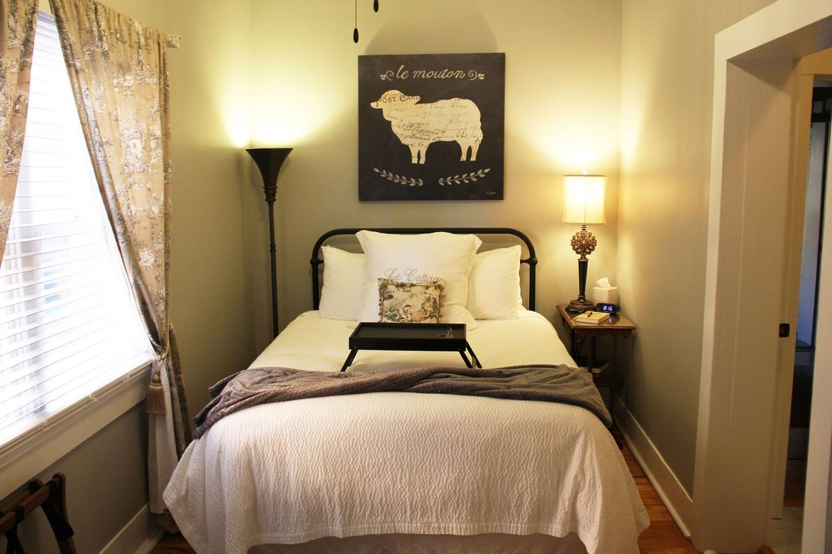 A neatly made bed with a tray, a lamp, and a wall art depicting a sheep.