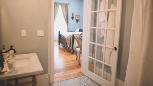 A bathroom with a marble sink, a wooden floor, and a door leading to a bedroom with a bed and curtains. - Boonville Luxury Lodging (Boonville)