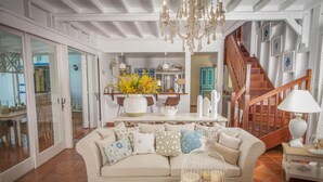 A spacious living room with a beige sofa, a chandelier, and a staircase leading to an upper level. - Luxury Villa in the French Carribean with a stunning view (Vieux Fort)