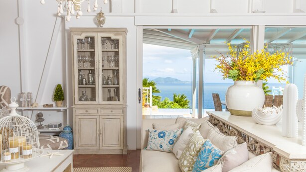 A cozy living room with a white sofa, a cabinet with glass doors, and a view of the sea. - Luxury Villa in the French Carribean with a stunning view (Vieux Fort)