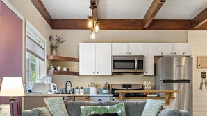 A cozy living room with a grey sofa, a round coffee table, and a kitchen in the background. - The GreenHouse - walk to the heart of Palmer, AK (Palmer)