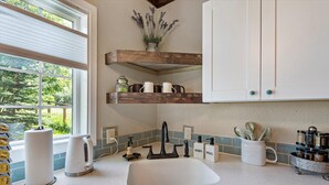 A kitchen with a white sink, wooden shelves, and a window with a view of greenery. - The GreenHouse - walk to the heart of Palmer, AK (Palmer)