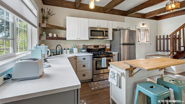 A kitchen with white cabinets, stainless steel appliances, a wooden table, and teal stools. - The GreenHouse - walk to the heart of Palmer, AK (Palmer)