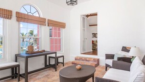 Ein sonnendurchflutetes Zimmer mit einem Korbstuhl, einem weißen Sofa und Blick ins Freie.