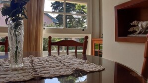 A dining area with a reflective table, lace curtains, a vase with flowers, and framed artwork on the wall. - Agradável Apartamento 2quartos Próximo ao Lago Negro a 4min do Centro (Gramado)
