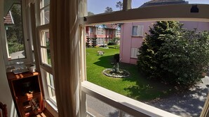 A room with a large window overlooking a well-maintained garden and neighboring buildings. - Agradável Apartamento 2quartos Próximo ao Lago Negro a 4min do Centro (Gramado)