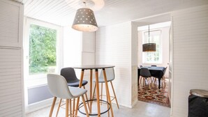 A room with a round table and two chairs, a hanging lamp, and a view of a garden through a window. - The royal escape (Saint-Benoît-la-Forêt)